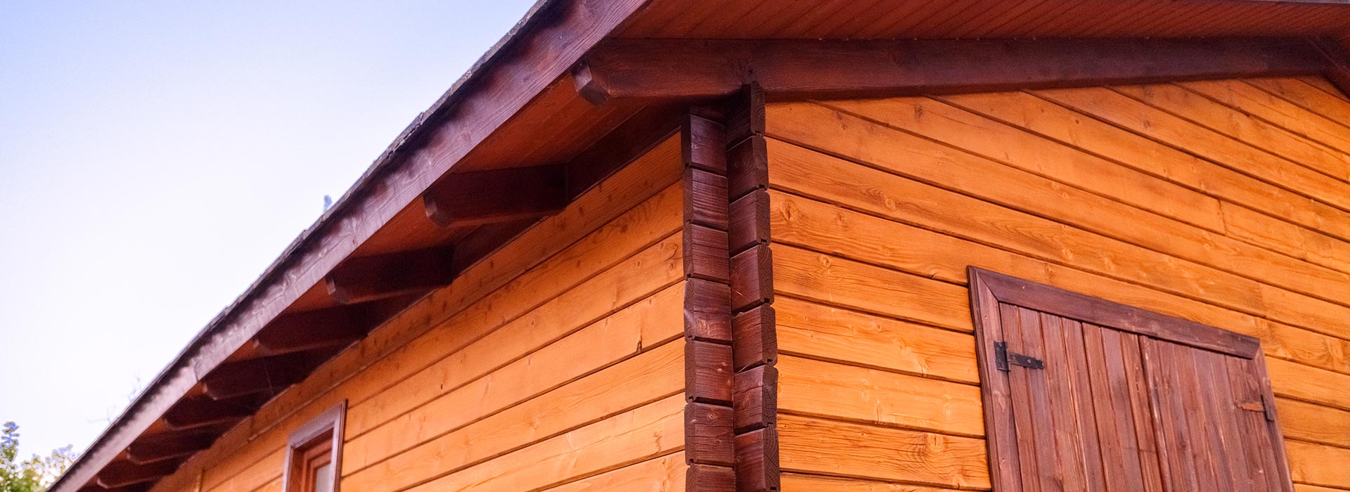 Wooden cabin corner with log siding and a wooden door against a clear sky.